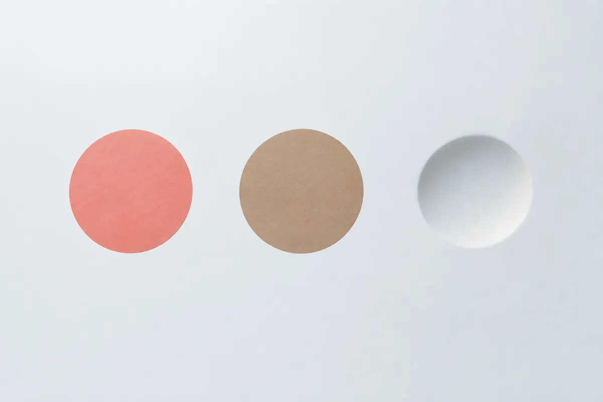 Three marks on a smooth pale surface: a flat pink-red disc, a flat light-brown disc and a small shadowed dip in the surface